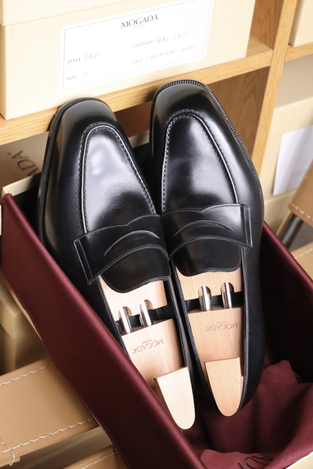 A pair of black leather loafers with a decorative strap, displayed in a burgundy box.