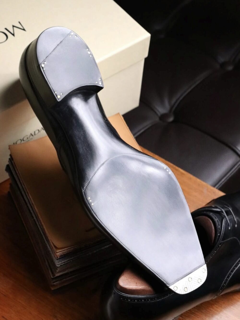 A black leather shoe sole with a gray rubber heel and metal studs on a wooden surface.