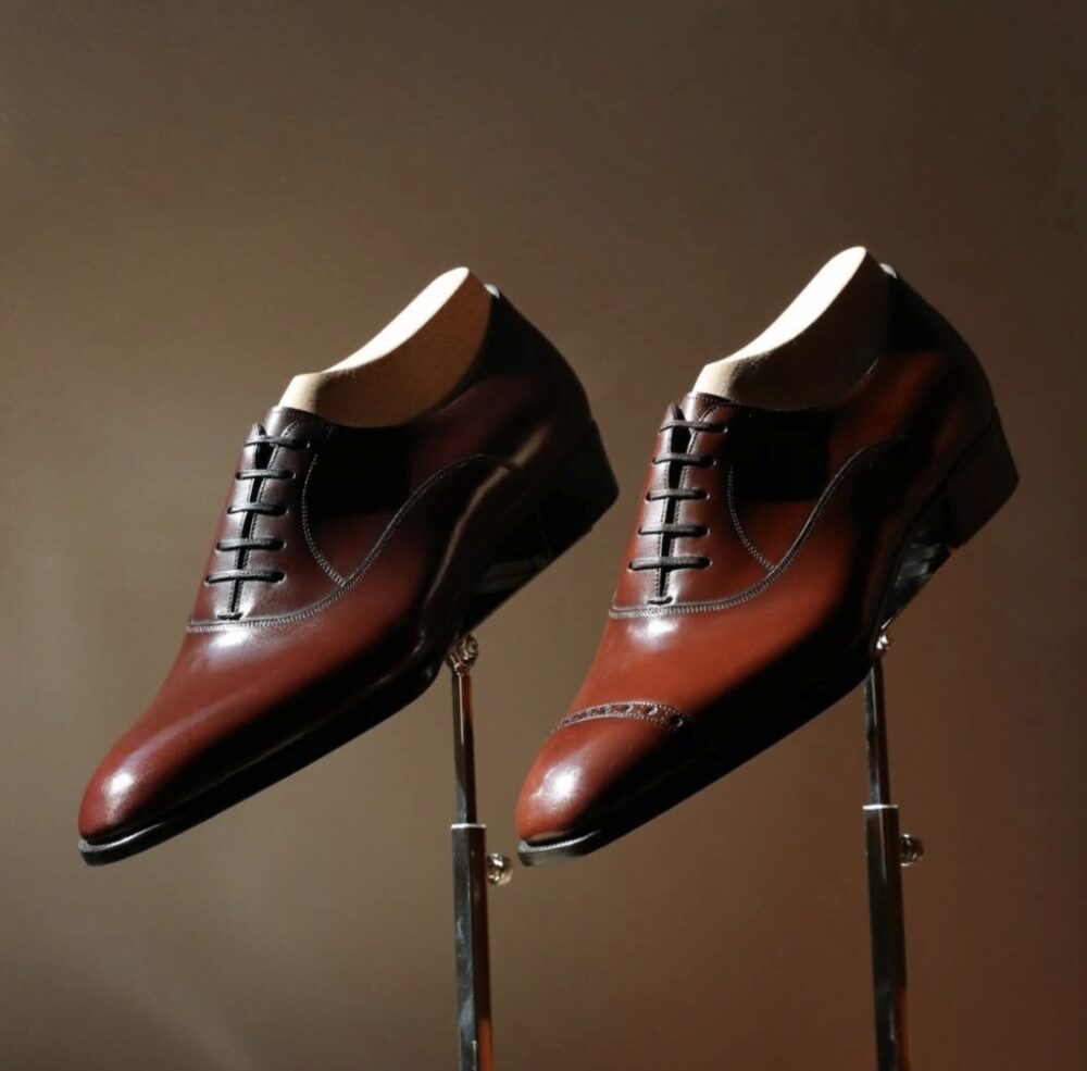 A pair of polished brown leather dress shoes with pointed toes and decorative lacing.
