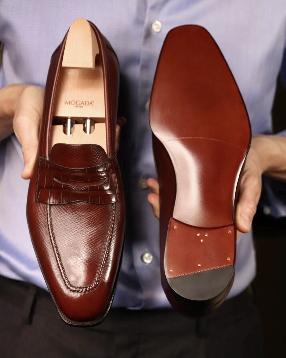 A person holds a pair of burgundy leather dress shoes, showcasing the textured upper and smooth sole.
