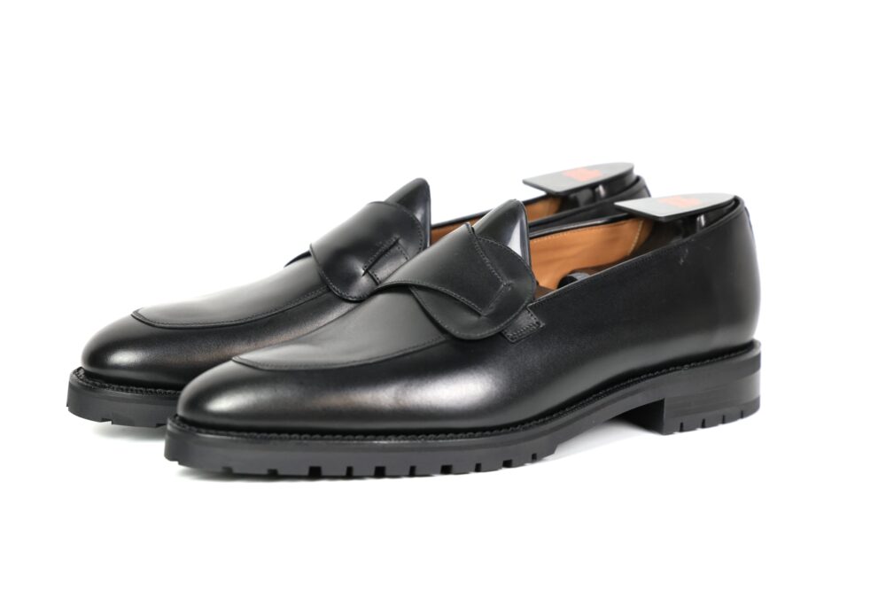 A pair of black leather loafers with a decorative flap and a rugged sole.