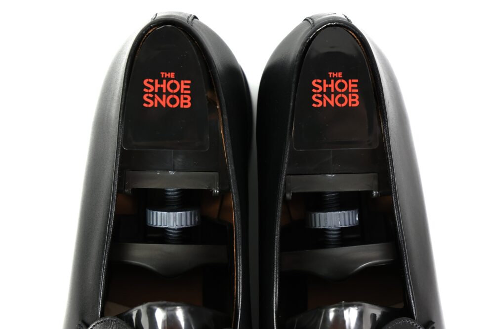A pair of black shoe trees with a visible logo reading "THE SHOE SNOB" in red.