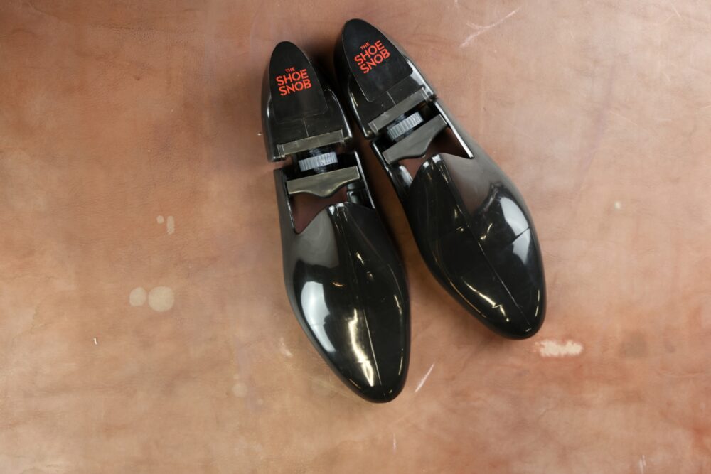 A pair of black shoe trees with "THE SHOE SNOB" printed in red on the toe section.