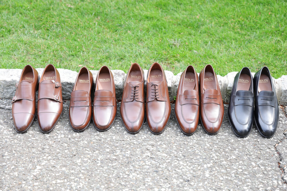 A lineup of eight pairs of leather shoes in shades of brown and black, featuring different styles including loafers and monk straps.