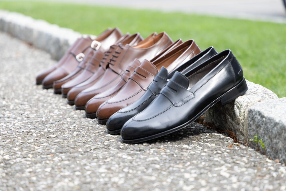 A line of eight formal shoes in various shades of brown and black, showcasing different styles and materials.