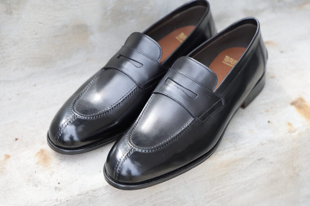 A pair of polished black leather loafers with decorative stitching.