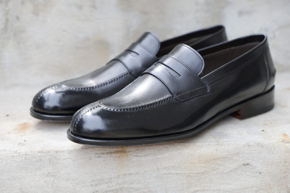 A pair of polished black leather loafers with a decorative seam across the top.