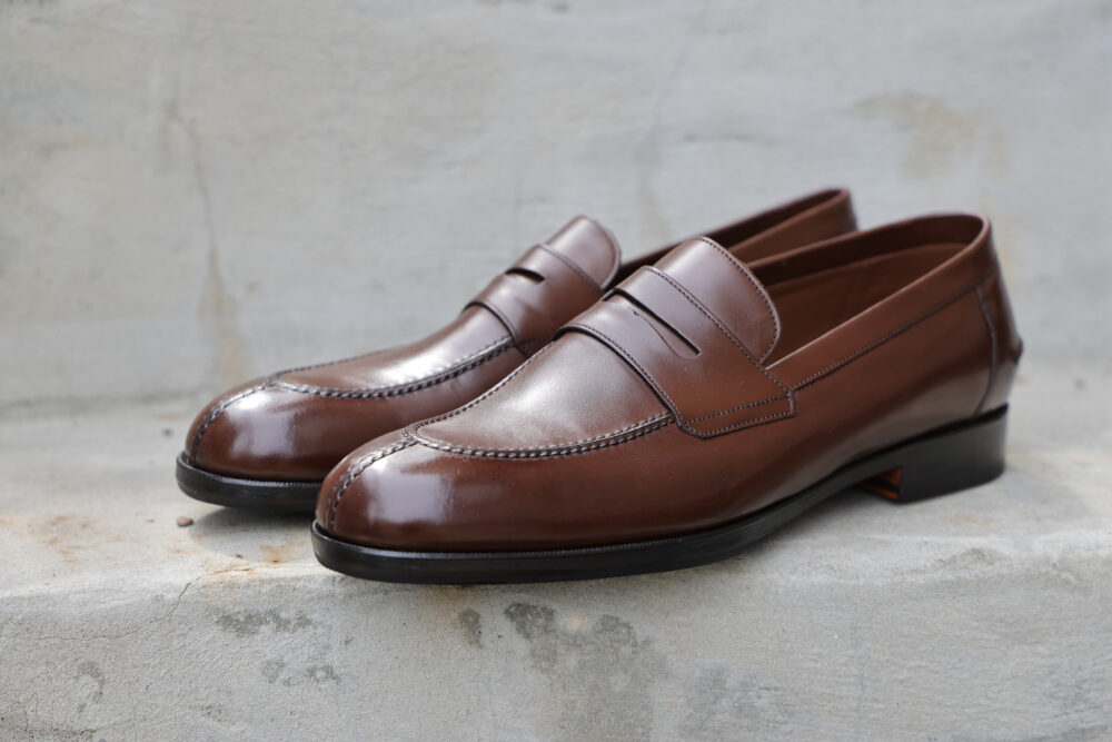 A pair of polished brown leather loafers with a decorative strap across the upper.