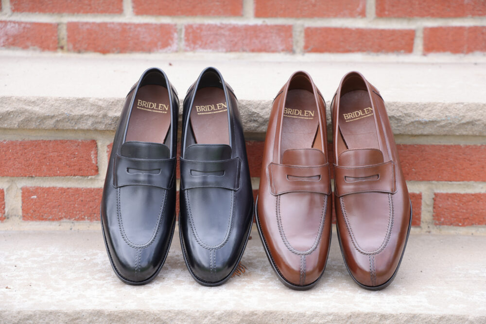 A pair of black and brown leather loafers with a slip-on design, featuring a decorative strap.