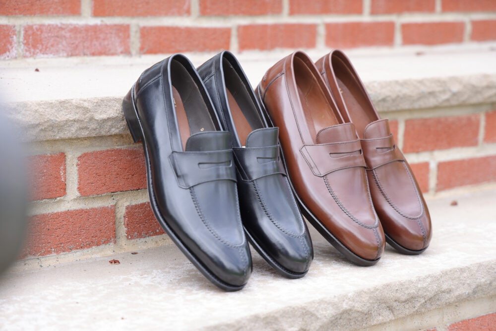 A pair of leather loafers in black and brown are displayed side by side.