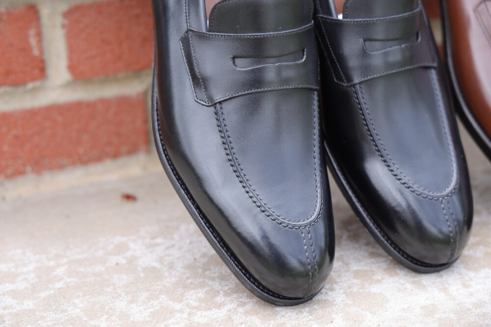 A close-up of polished black leather loafers with decorative stitching.