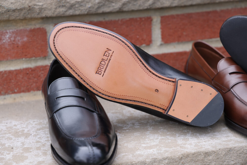 A close-up of a black leather shoe with a tan leather sole, featuring the brand name "Bridlen" embossed on it.