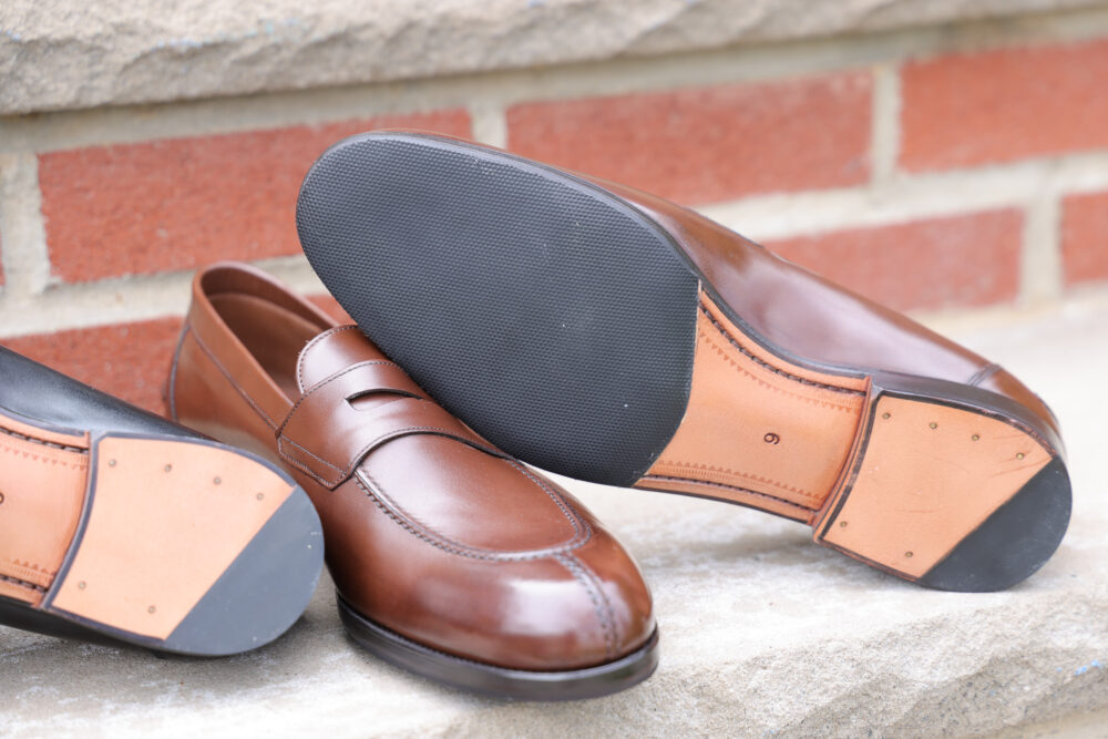 A pair of brown leather loafers with black rubber soles, showcasing their detailed stitching and materials.