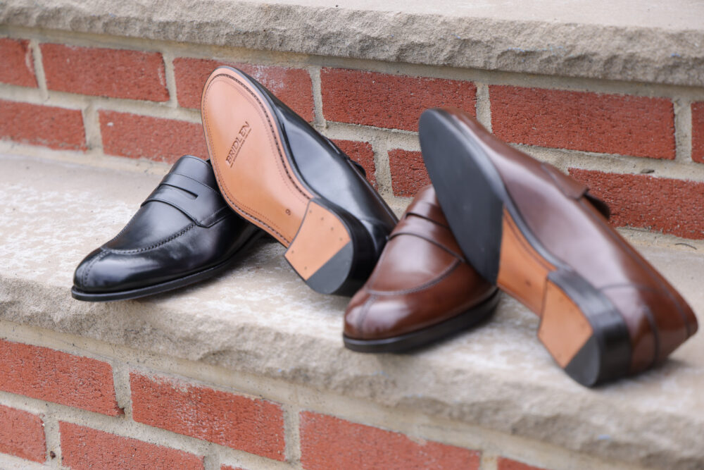 A pair of leather shoes, one black and one brown, displayed on a stone surface.