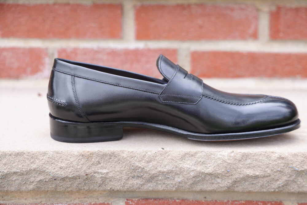 A polished black leather loafer shoe with a slight heel.