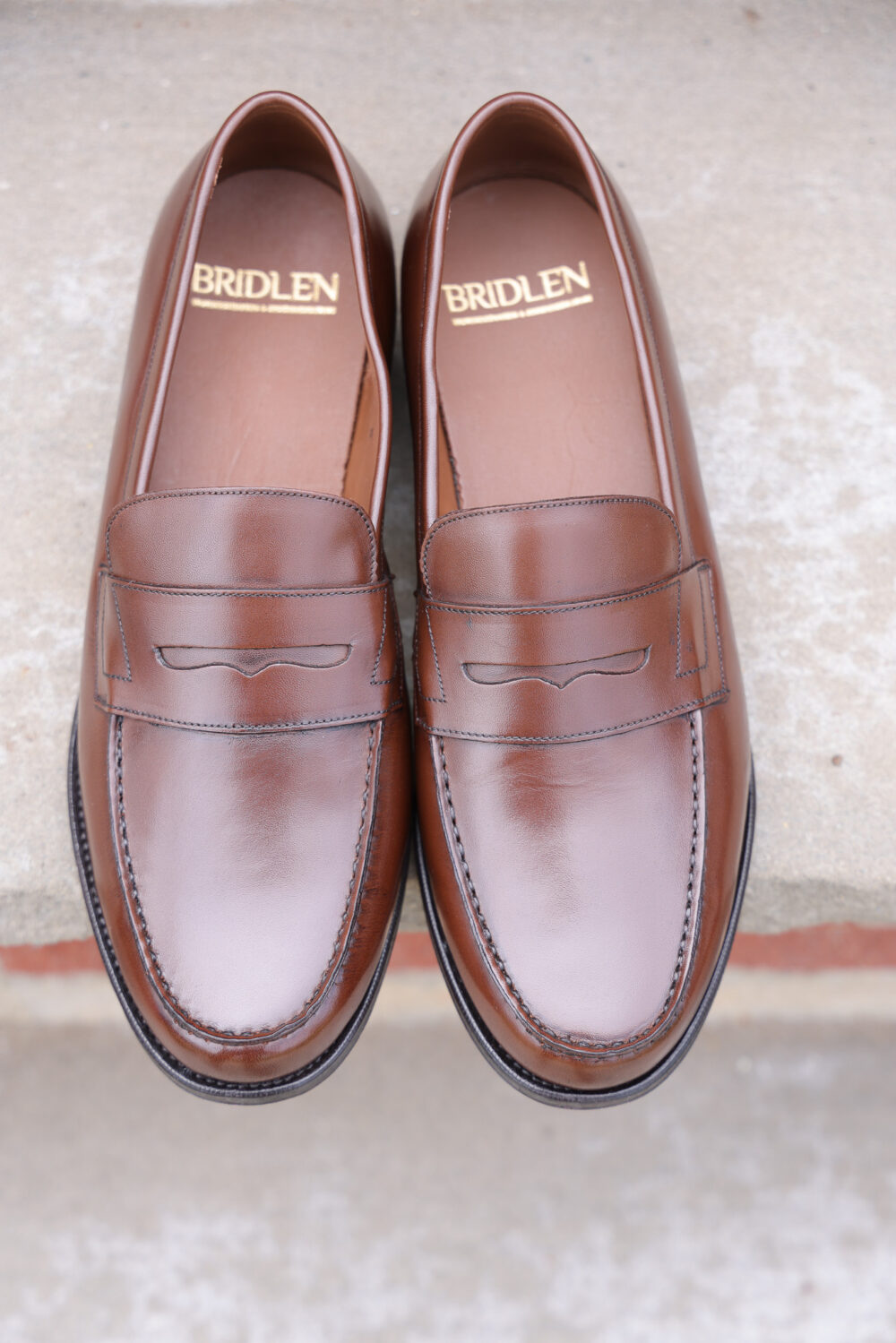 A pair of brown leather loafers with a decorative stitching detail and the brand name "Bridlen" visible inside.