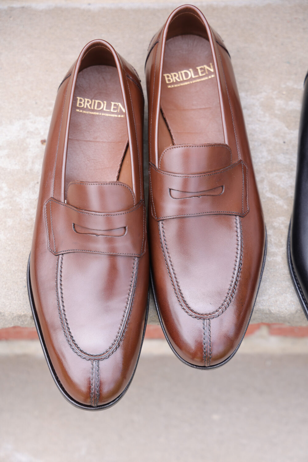 A pair of brown leather loafers with decorative stitching and a small strap detail.