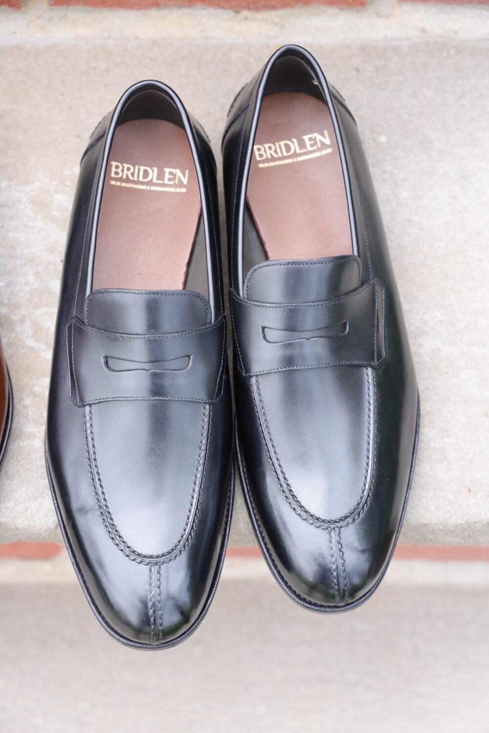A pair of black leather loafers with a decorative front strap and stitched detailing.