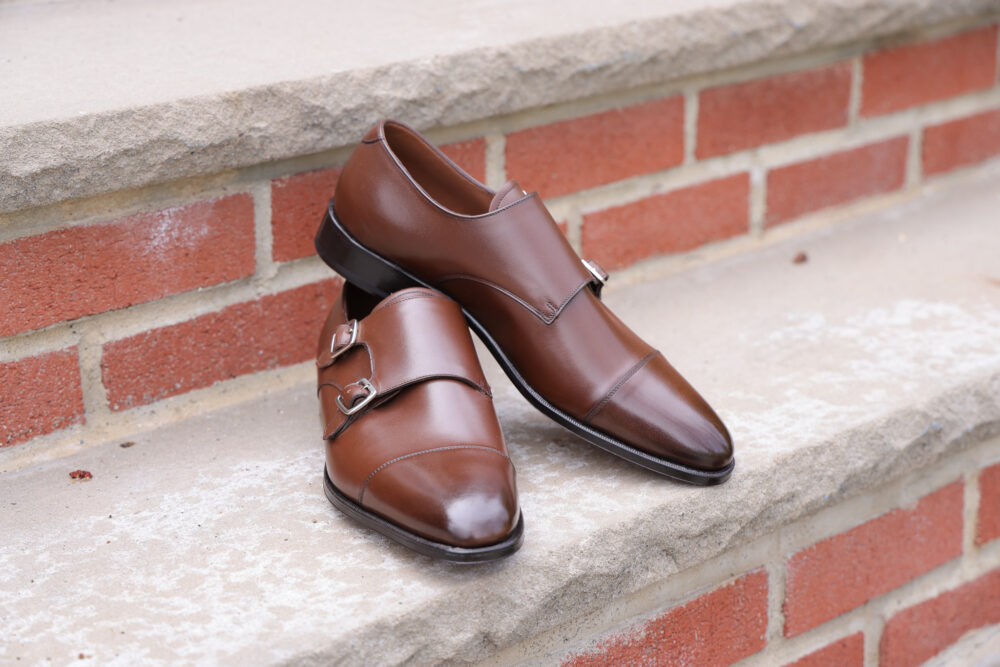 A pair of polished brown leather dress shoes with double buckles, resting on a stone surface.