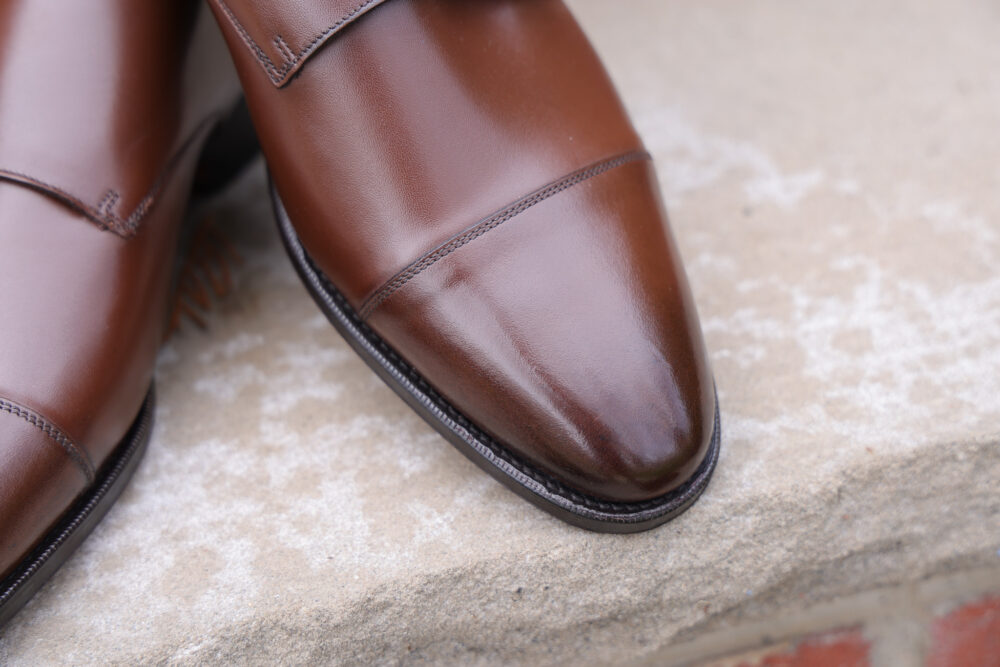 A close-up of polished brown leather dress shoes with a pointed toe and decorative stitching.