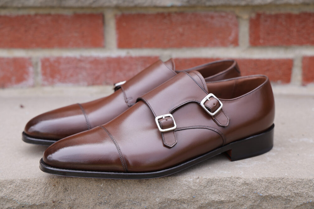 A pair of polished brown leather shoes with silver buckles.