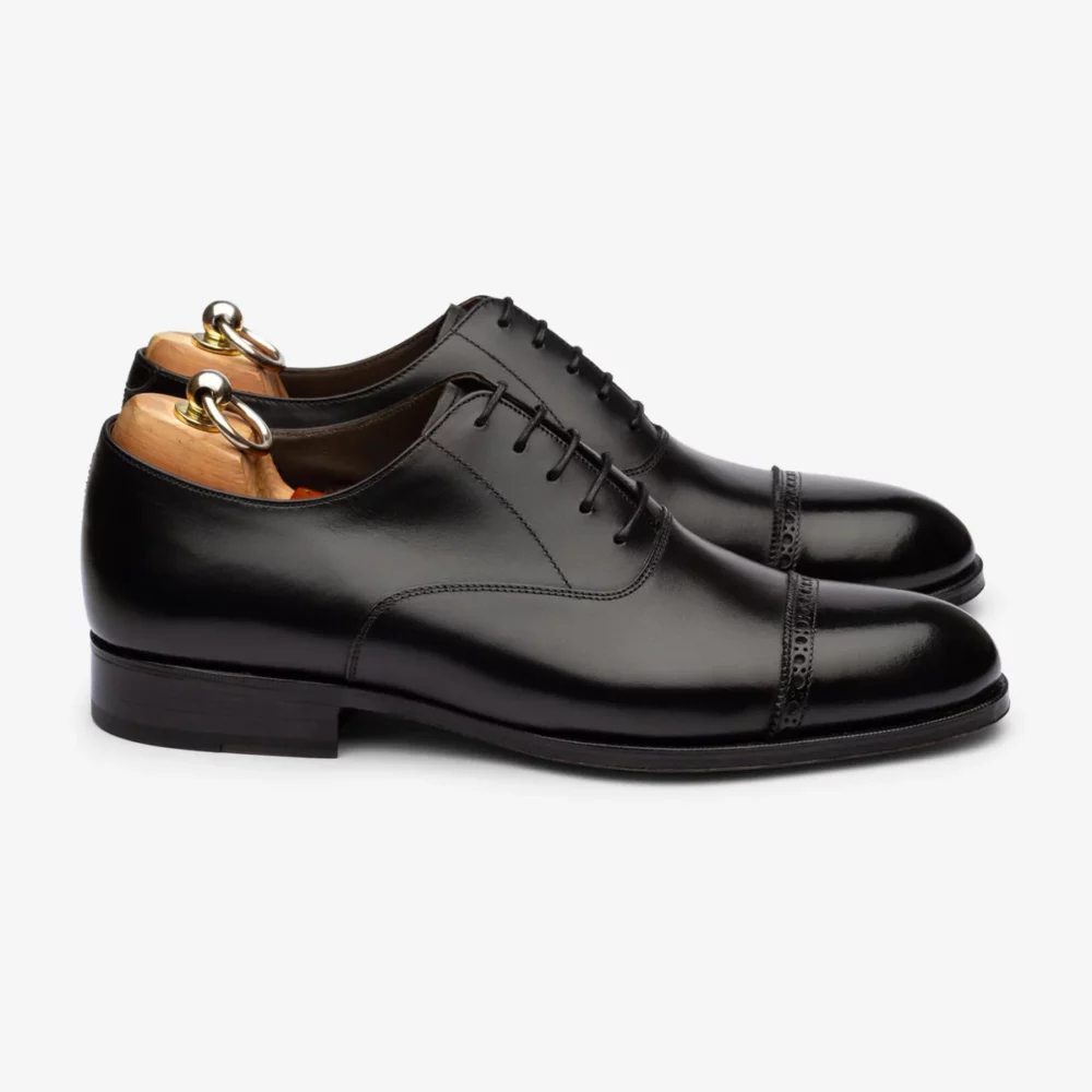 A pair of black leather dress shoes with a cap toe and wooden shoe trees.