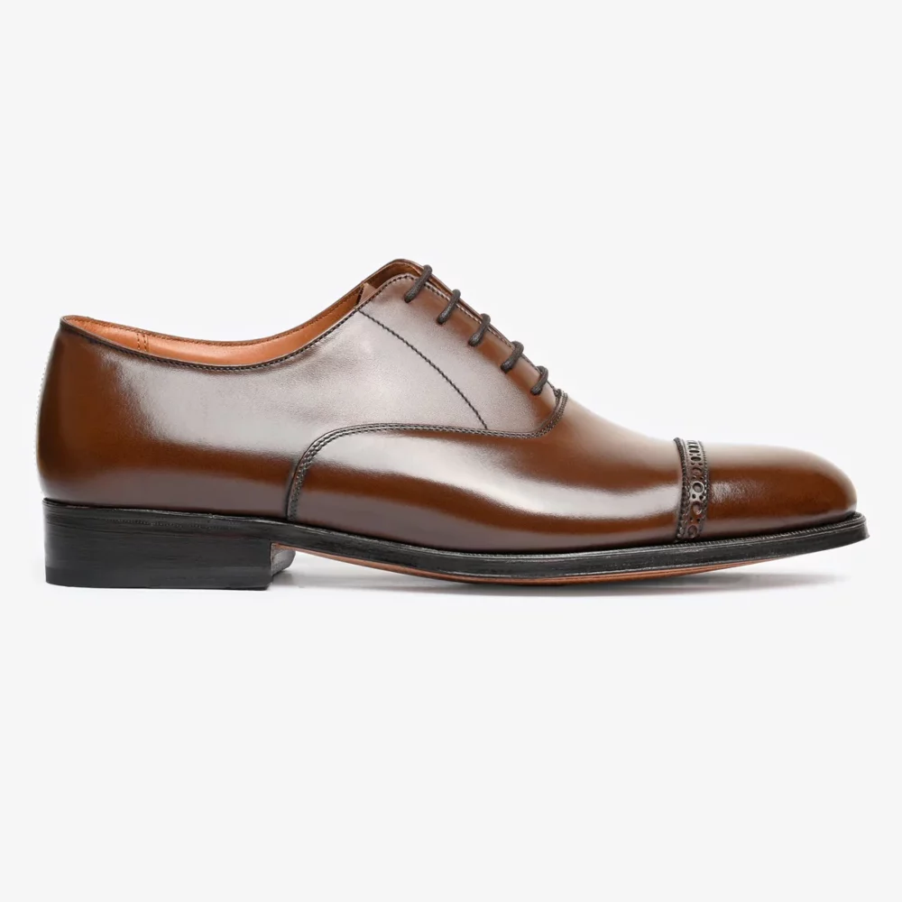 A polished brown leather dress shoe with a rounded toe and decorative detailing on the cap.