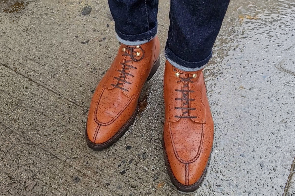 Brown leather shoes with laces, displaying water droplets, worn with dark jeans.