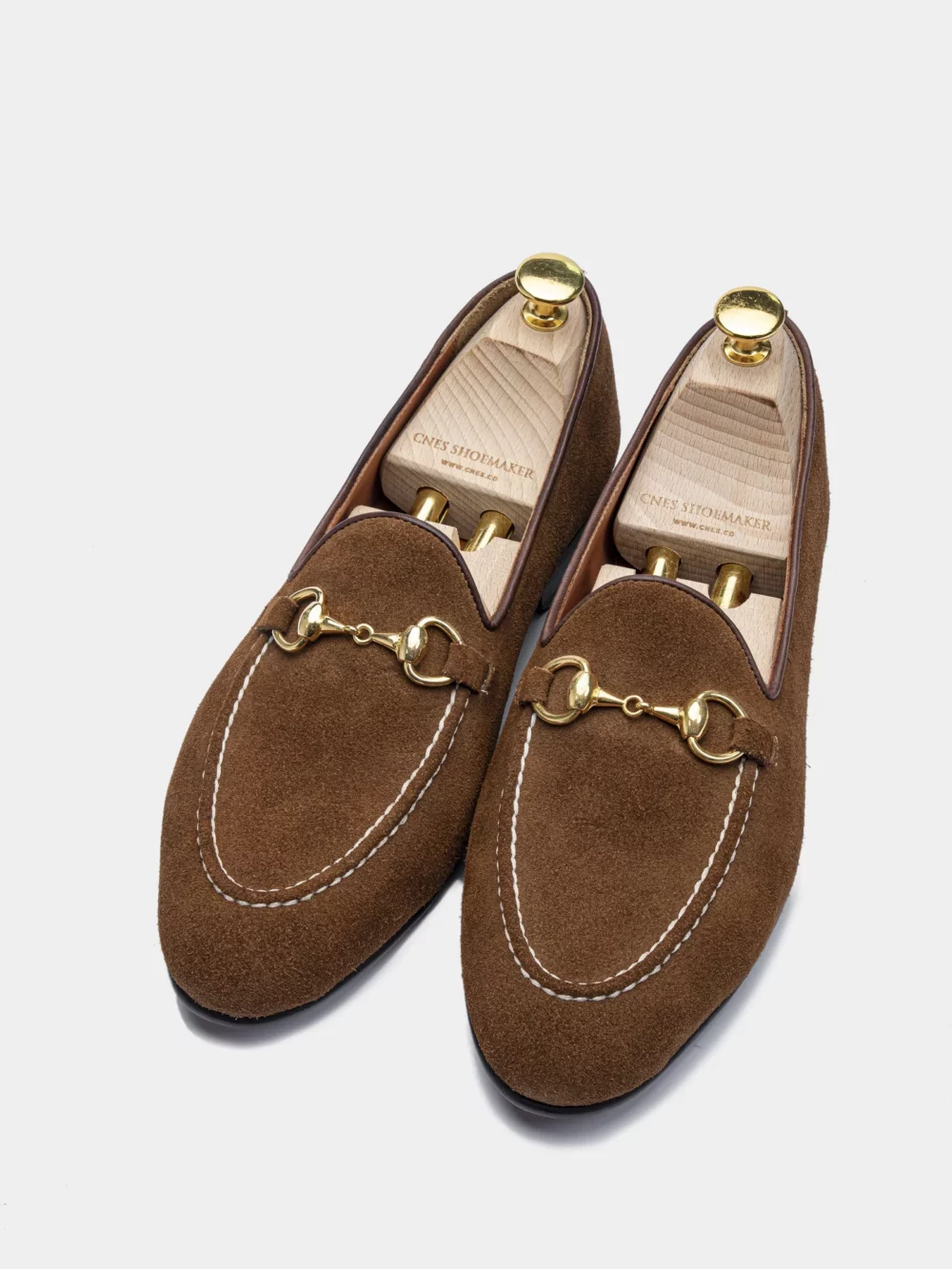 Brown suede loafers with gold detailing and white stitching.
