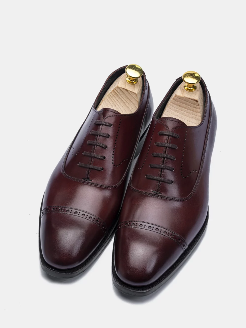 A pair of polished burgundy leather dress shoes with decorative stitching and wooden shoe trees.