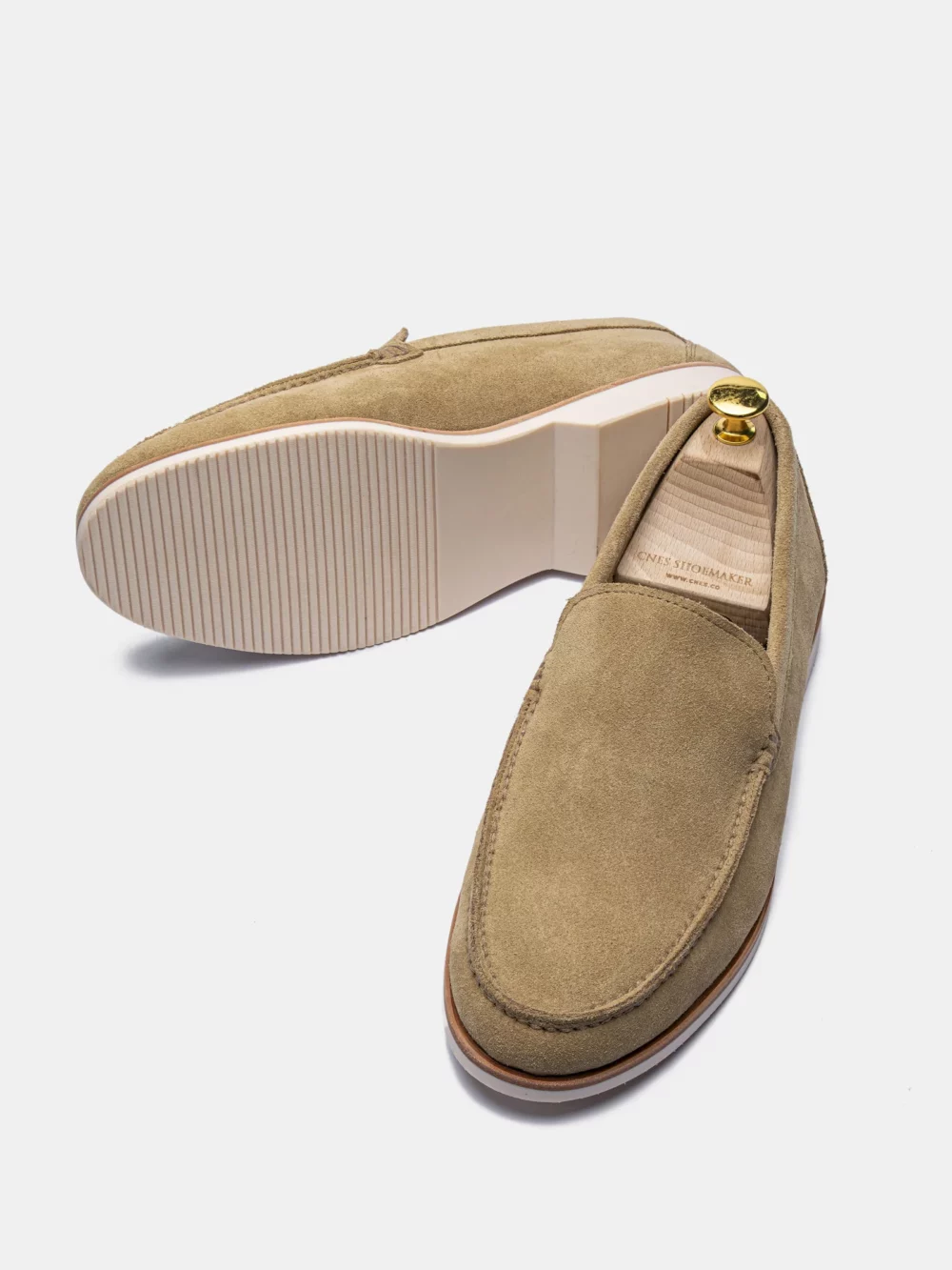 A pair of tan suede loafers with a light-colored sole and a gold accent on the heel.