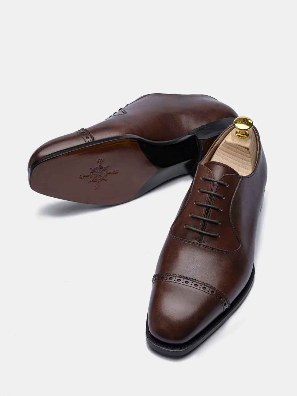 A pair of brown leather dress shoes with a pointed toe and decorative perforations.