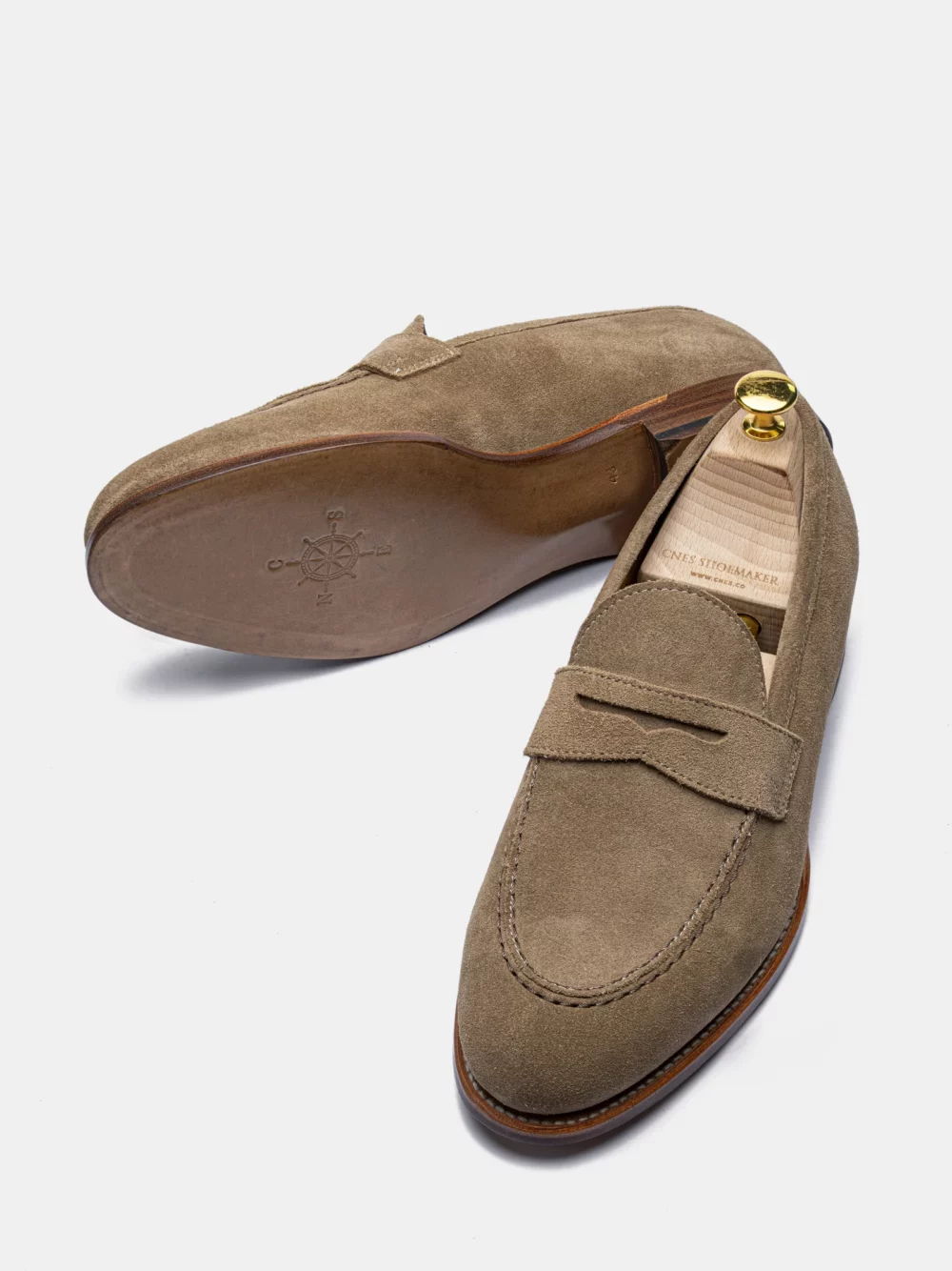 A pair of brown suede loafers with a decorative strap and a gold shoehorn.