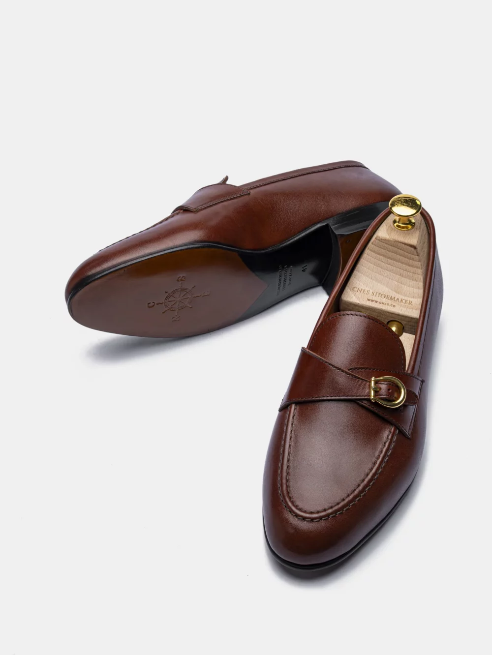 A pair of brown leather loafers featuring a decorative gold buckle.