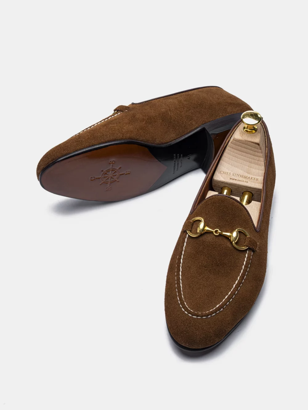 Brown suede loafers in the CNES Spring Sale 2026 with a gold-tone chain detail and white stitching.