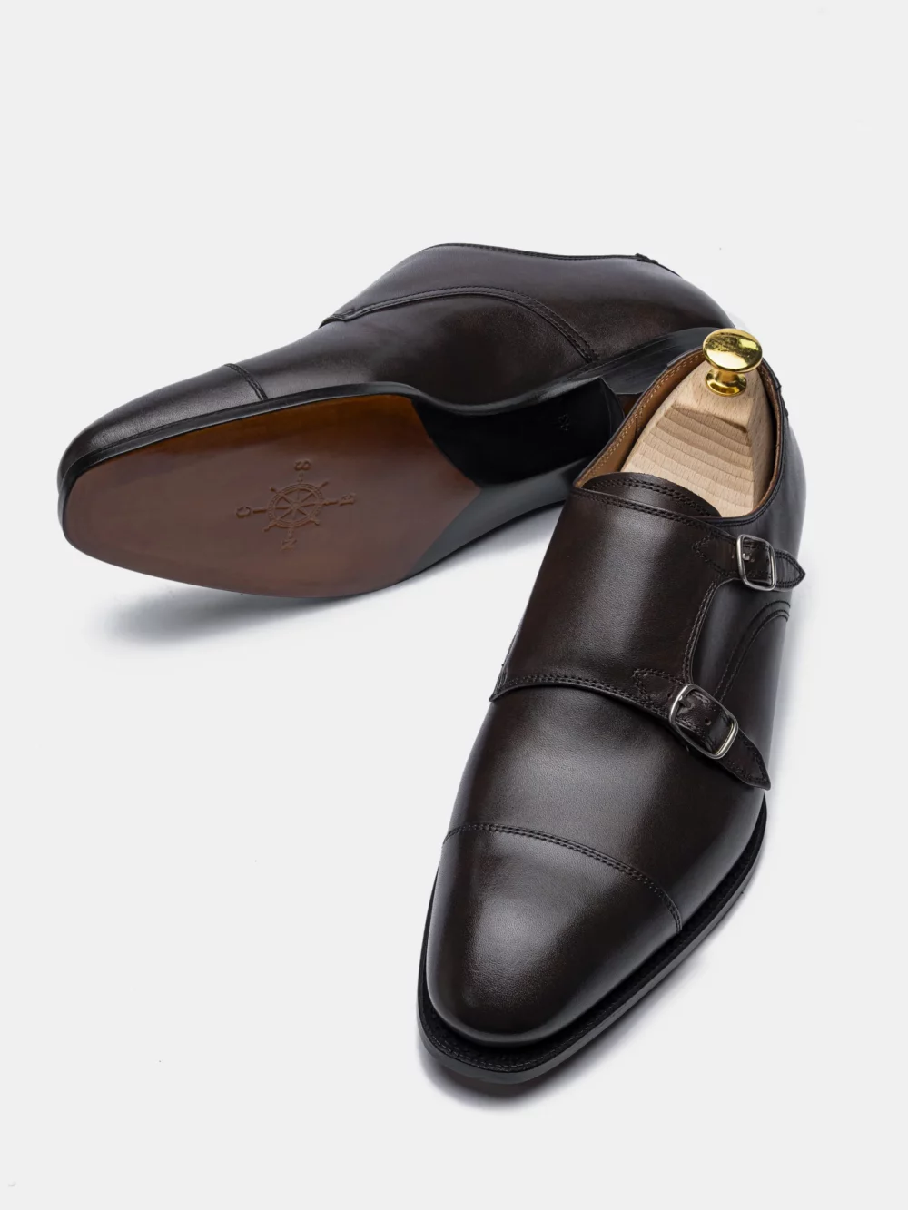 A pair of CNES dark brown leather dress shoes with a buckle detail and a wooden shoe tree