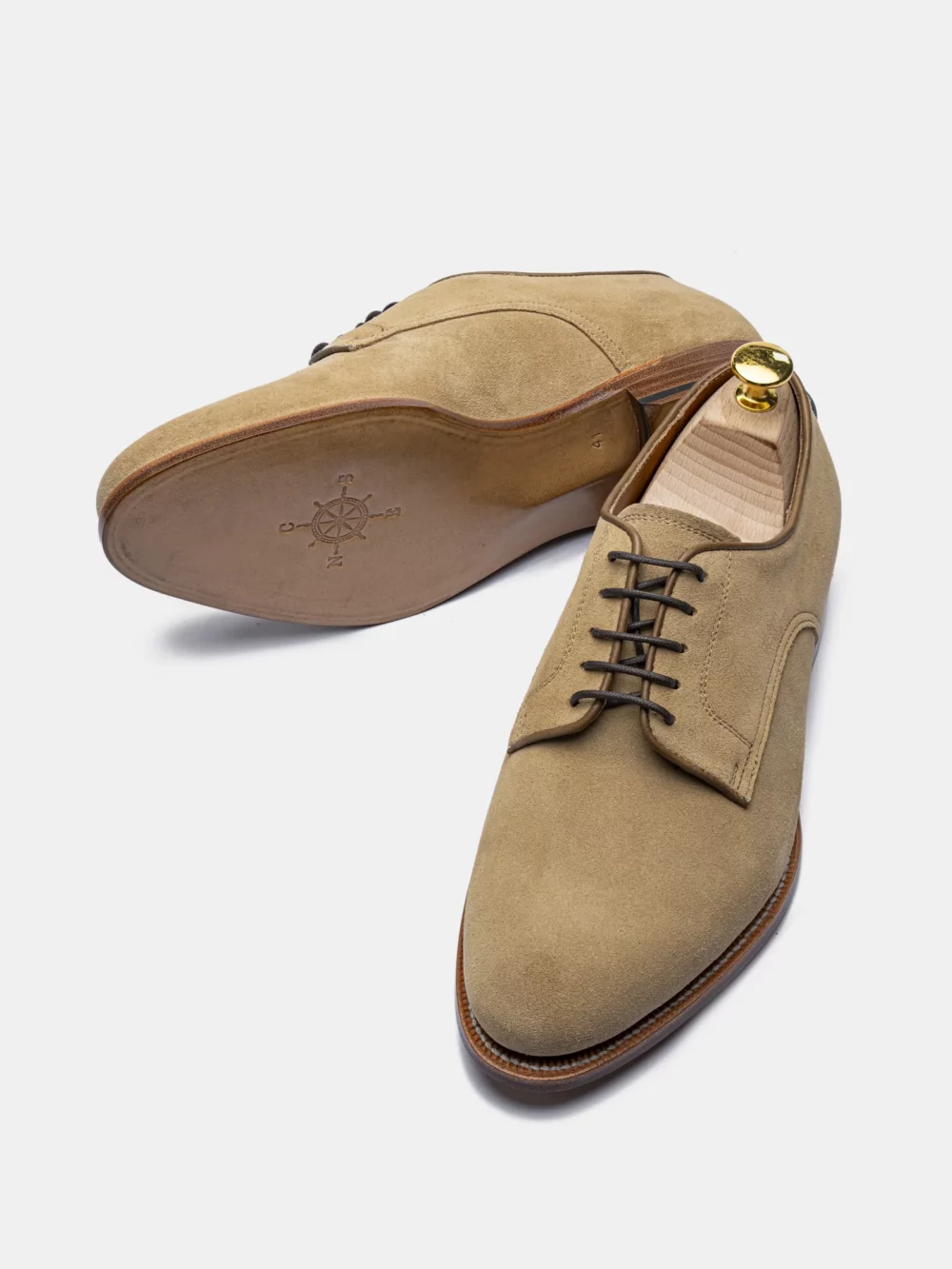 A pair of tan suede dress shoes with brown laces and a gold shoehorn.