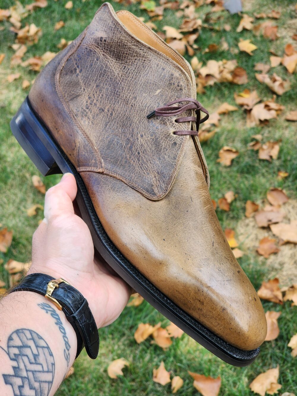 A person holding a brown leather dress boot with a smooth finish and dark laces.