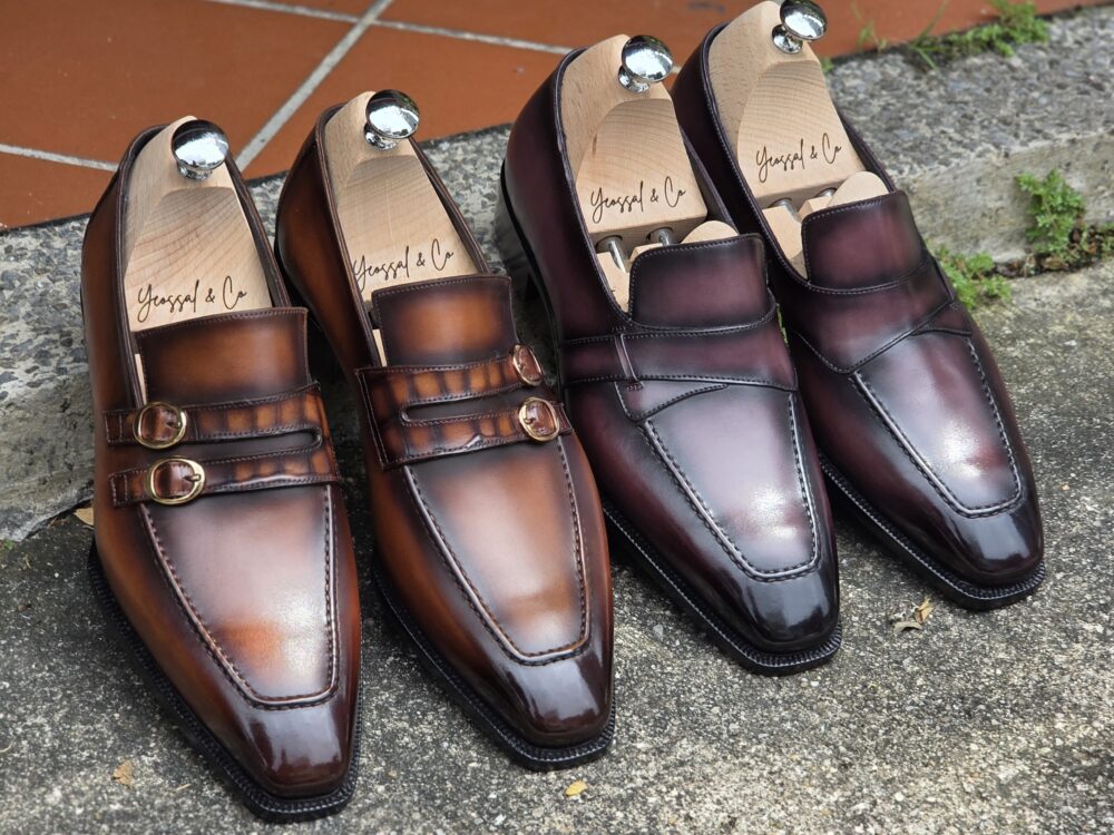 Two pairs of leather dress shoes in brown and burgundy, featuring sleek designs and decorative buckles.