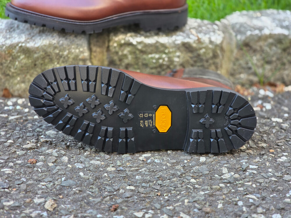 The image shows the black rubber sole of a brown leather boot, featuring a Vibram logo.
