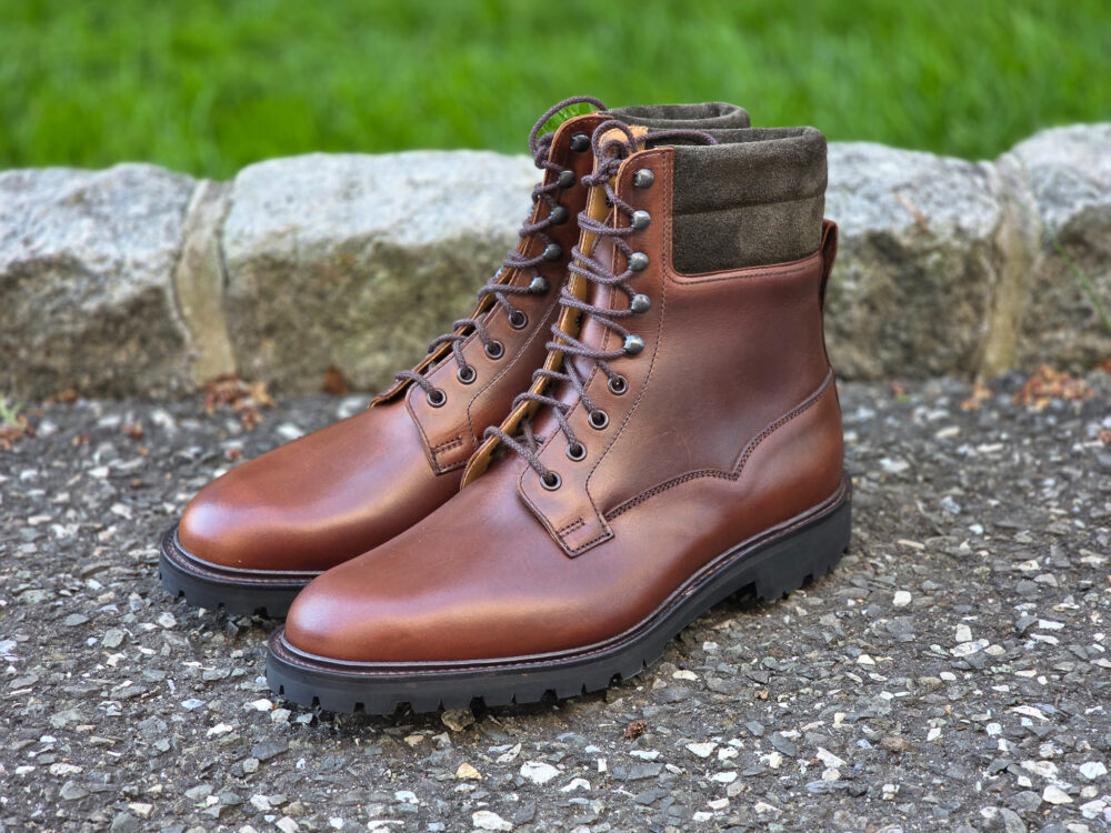 A pair of brown leather hiking boots with a sturdy sole and a soft, dark green collar.