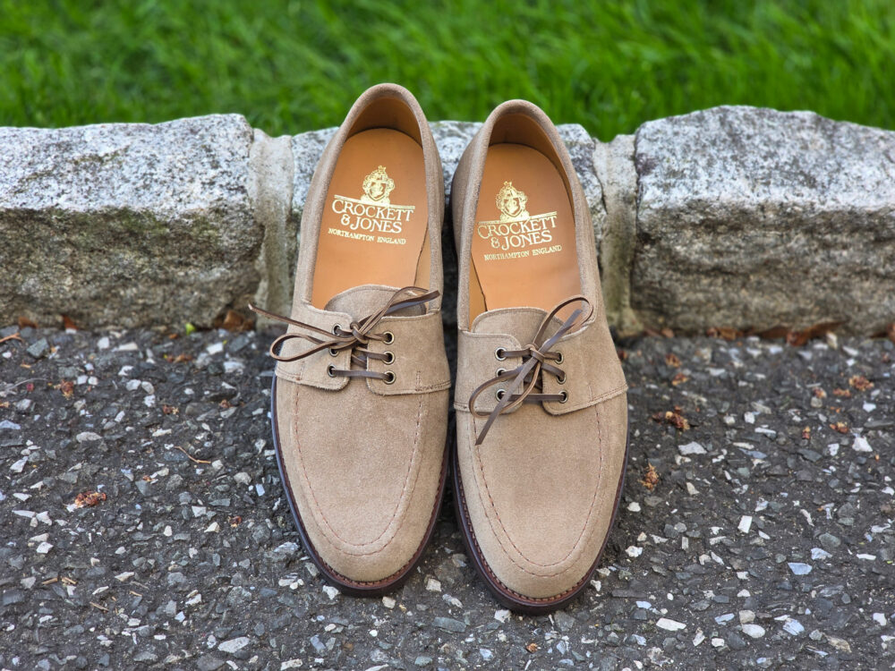 A pair of tan suede shoes with laces, featuring the brand name "Crockett & Jones" on the insoles.