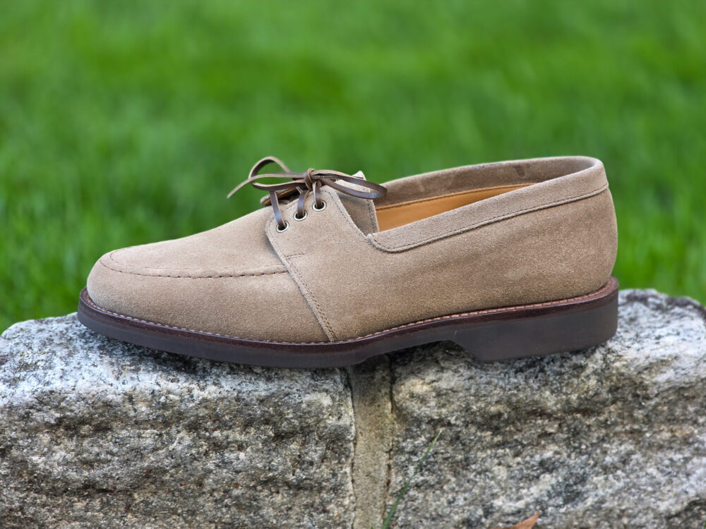 A tan suede shoe with brown laces resting on a stone surface.