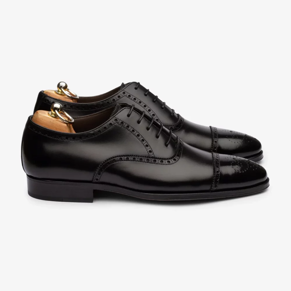 A pair of polished black leather dress shoes with decorative broguing and wooden shoe trees.