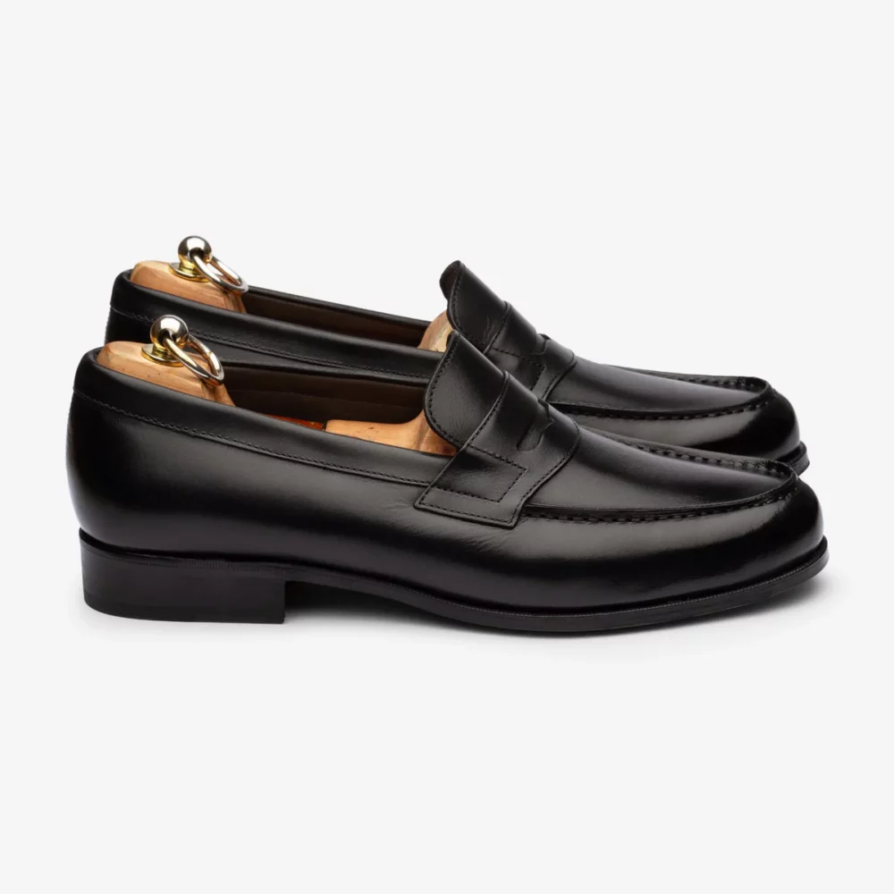 A pair of black leather loafers with a low heel and decorative stitching.