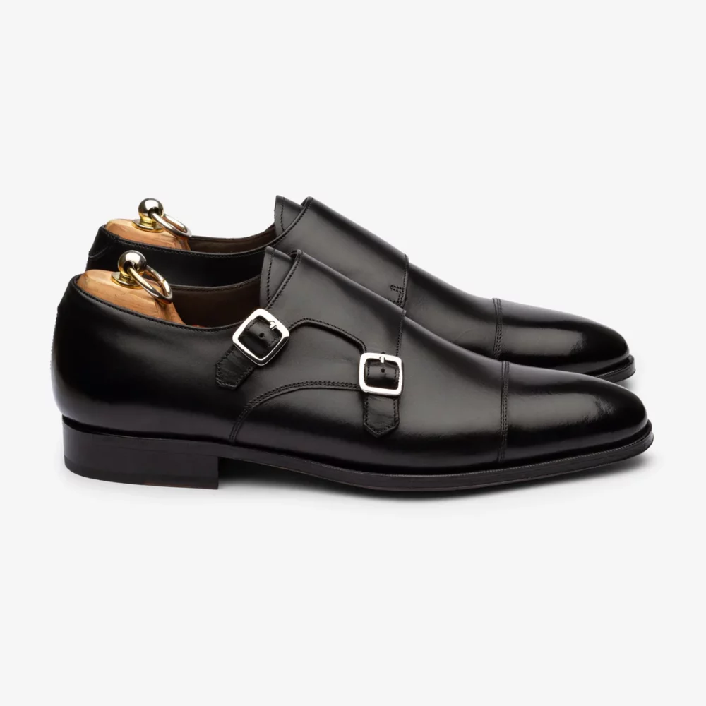A pair of shiny black leather shoes with double buckles and wooden shoe trees.