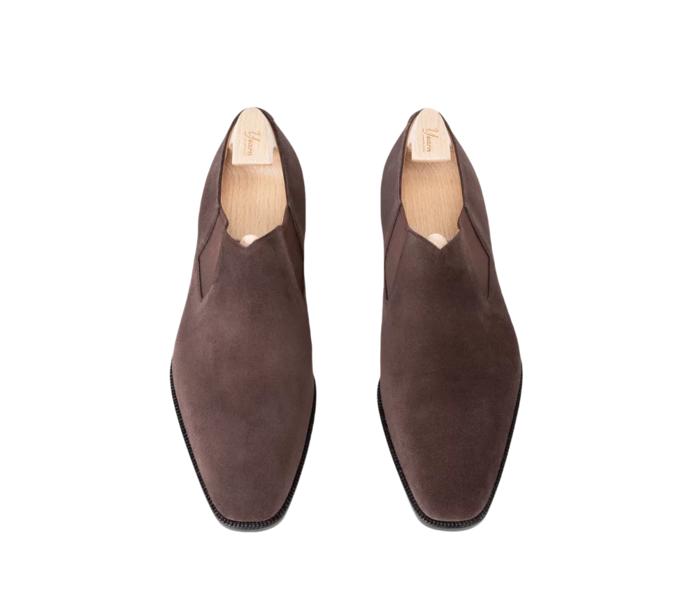 A pair of dark brown suede slip-on shoes with a pointed toe design.