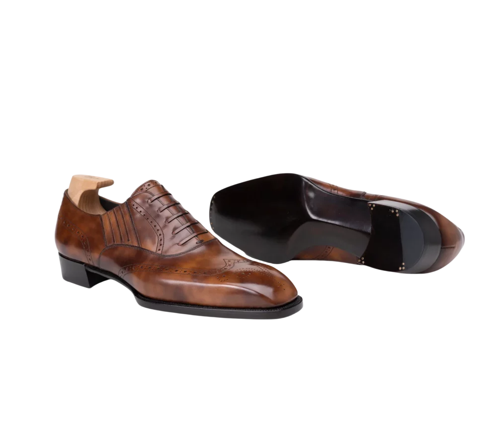 A pair of polished brown leather dress shoes with decorative broguing and a sleek black sole.