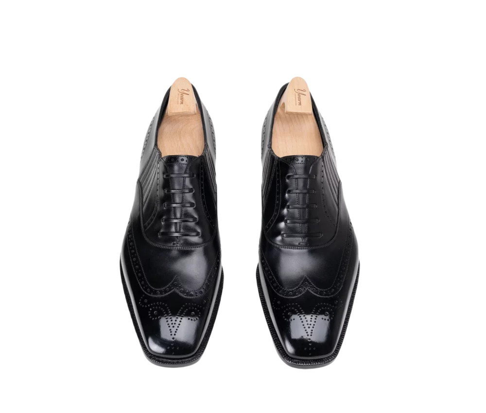 A pair of black leather dress shoes with a polished finish and decorative brogue detailing.