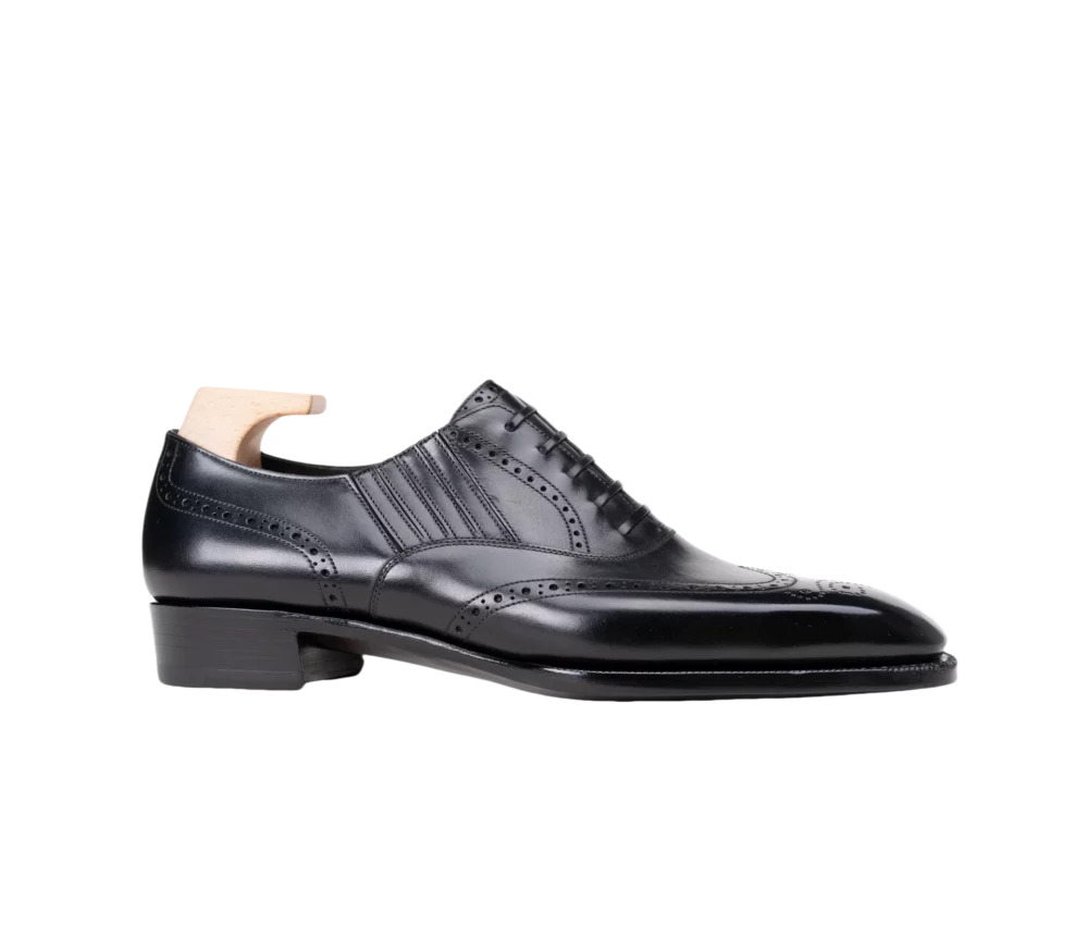 A black leather dress shoe with decorative perforations and a wooden shoe tree inserted.
